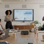 Business people, meeting and presentation on screen for data analytics, statistics and financial growth in boardroom. Professional leader, woman or analyst with monitor for graphs, charts and report MSP packaging and bundling strategies